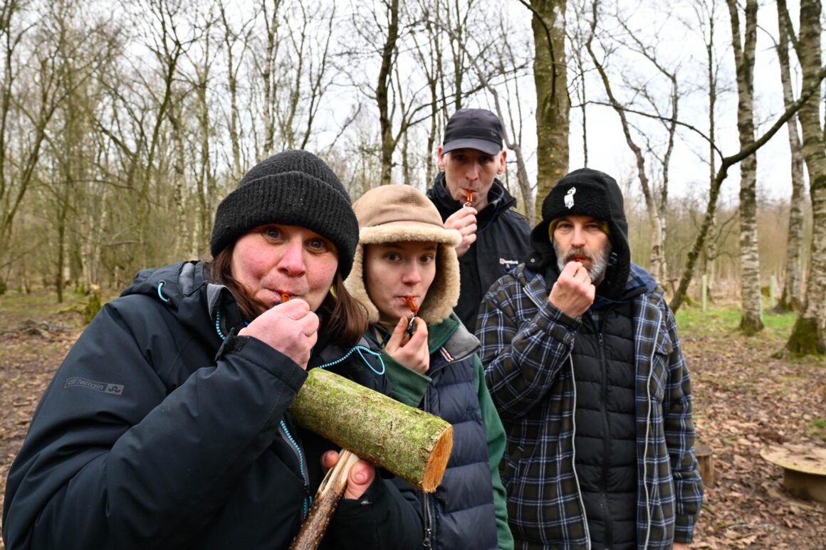Volunteers posing for a photograph blowing wooden whistles made during a woodland skills teaching session.