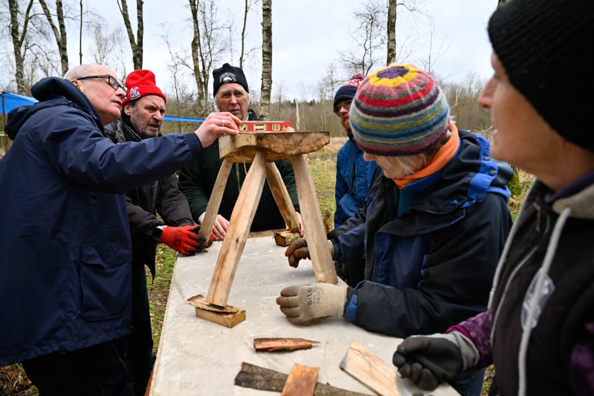 Volunteers using a spirit level on a newly constructed wooden bench to ensure that its legs are level.