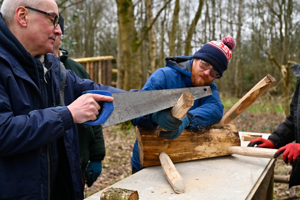 Volunteers sawing sections from the feet of a wooden bench to ensure that they are level.