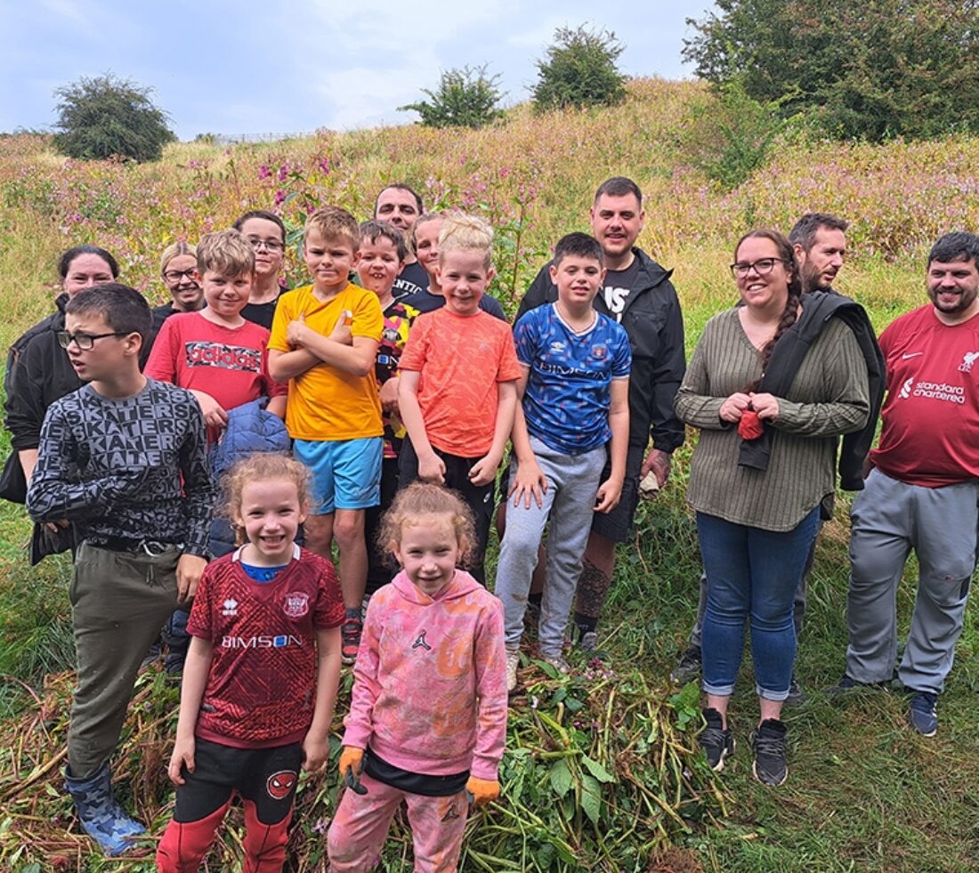 A large group of young people are posing for a photograph standing on a pile of uprooted Himalayan balsam after a day of balsam bashing at Petteril Vale in Carlisle.