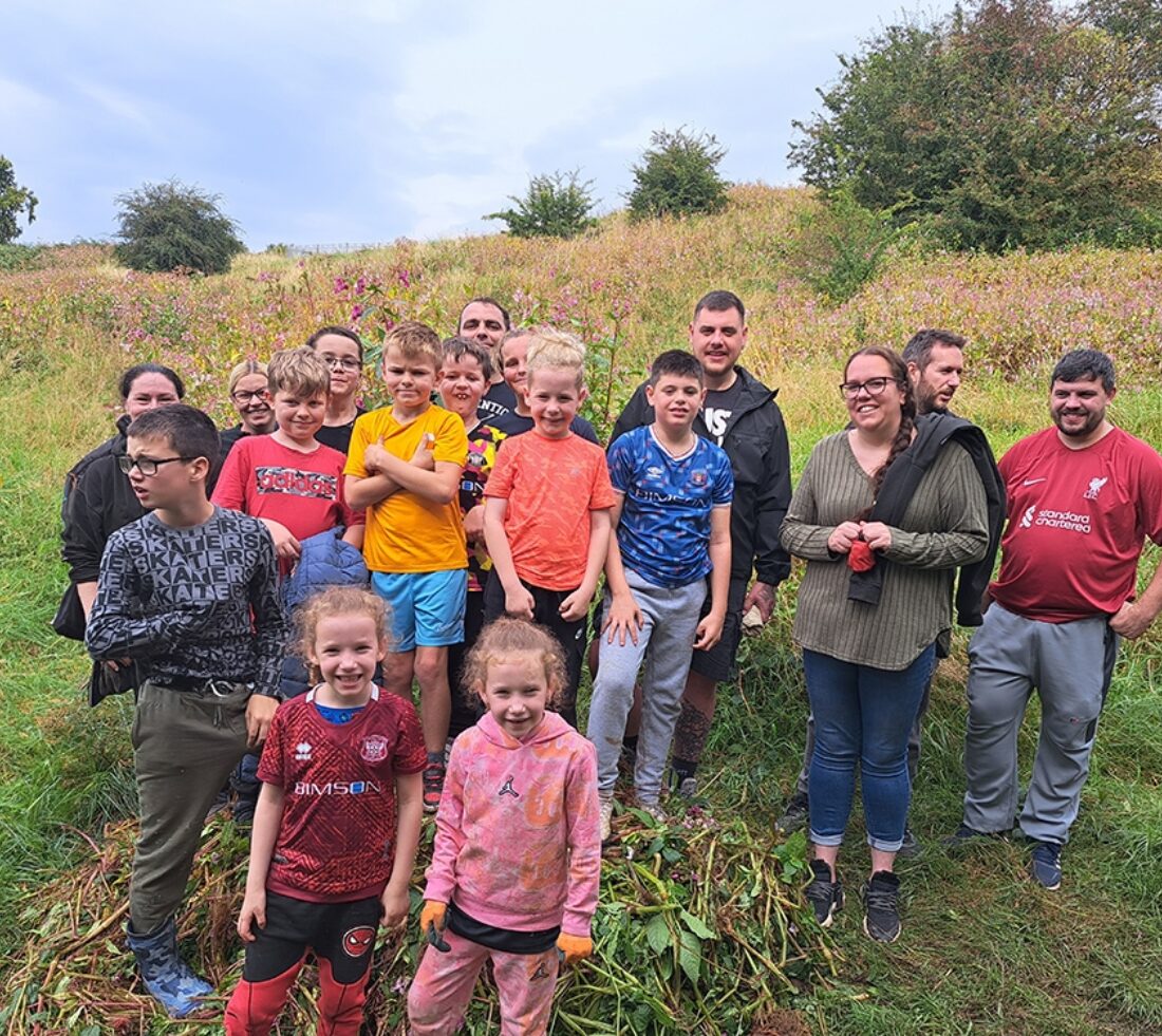 A large group of young people are posing for a photograph standing on a pile of uprooted Himalayan balsam after a day of balsam bashing at Petteril Vale in Carlisle.