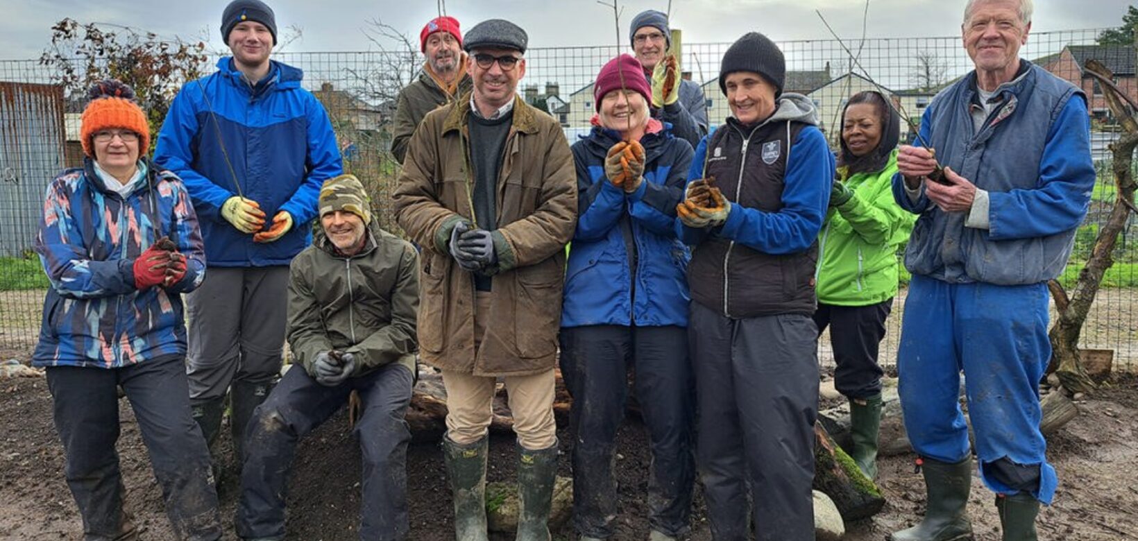 A group of volunteers standing on muddy ground and holding tree saplings post for a group photograph.
