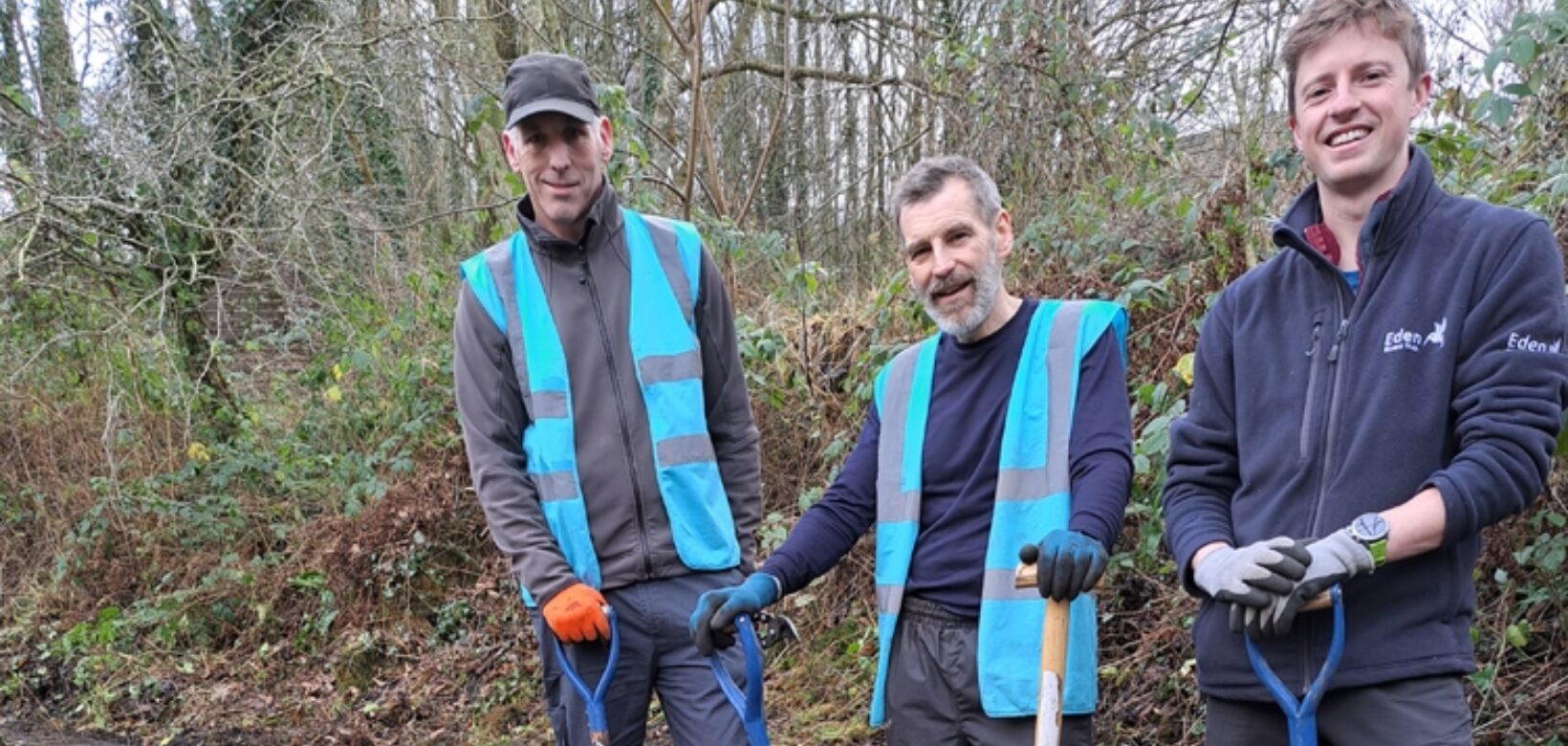 A group of three volunteers holding spades are standing next to a cleared section of stonework forming part of a former railway turntable.