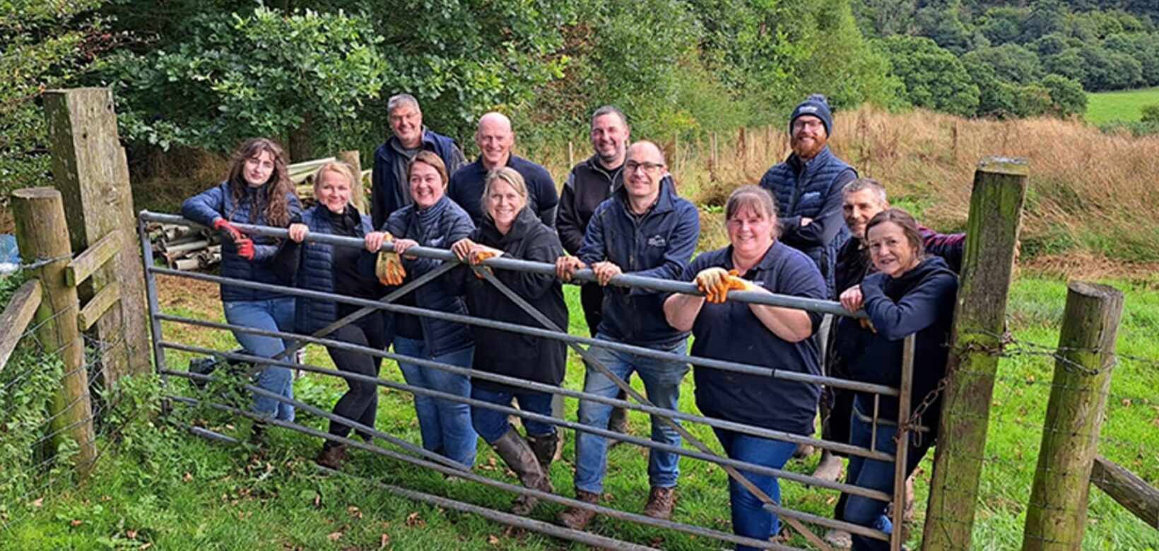 A group of volunteers posing for a photograph, lined up along a metal farm gate.