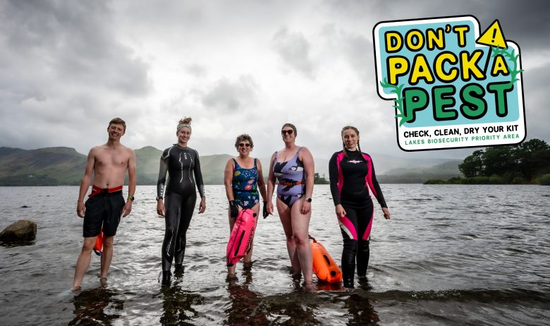 Five water users standing in shallow water at the lakes edge. Dressed in shorts, wetsuits and swimming costumes. A graphic in the corner of the image reads: Don't pack a pest.
