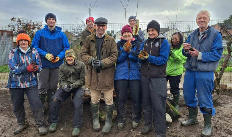 A group of volunteers standing on muddy ground and holding tree saplings post for a group photograph.