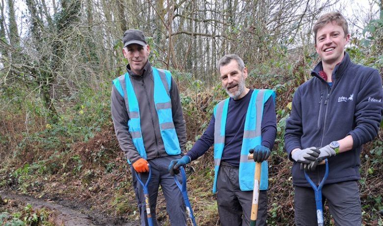 A group of three volunteers holding spades are standing next to a cleared section of stonework forming part of a former railway turntable.