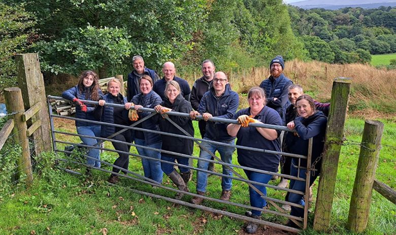 A group of volunteers posing for a photograph, lined up along a metal farm gate.