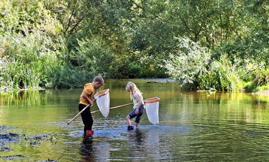 Two young people with nets and wellies wading in a river, looking for aquatic fauna.