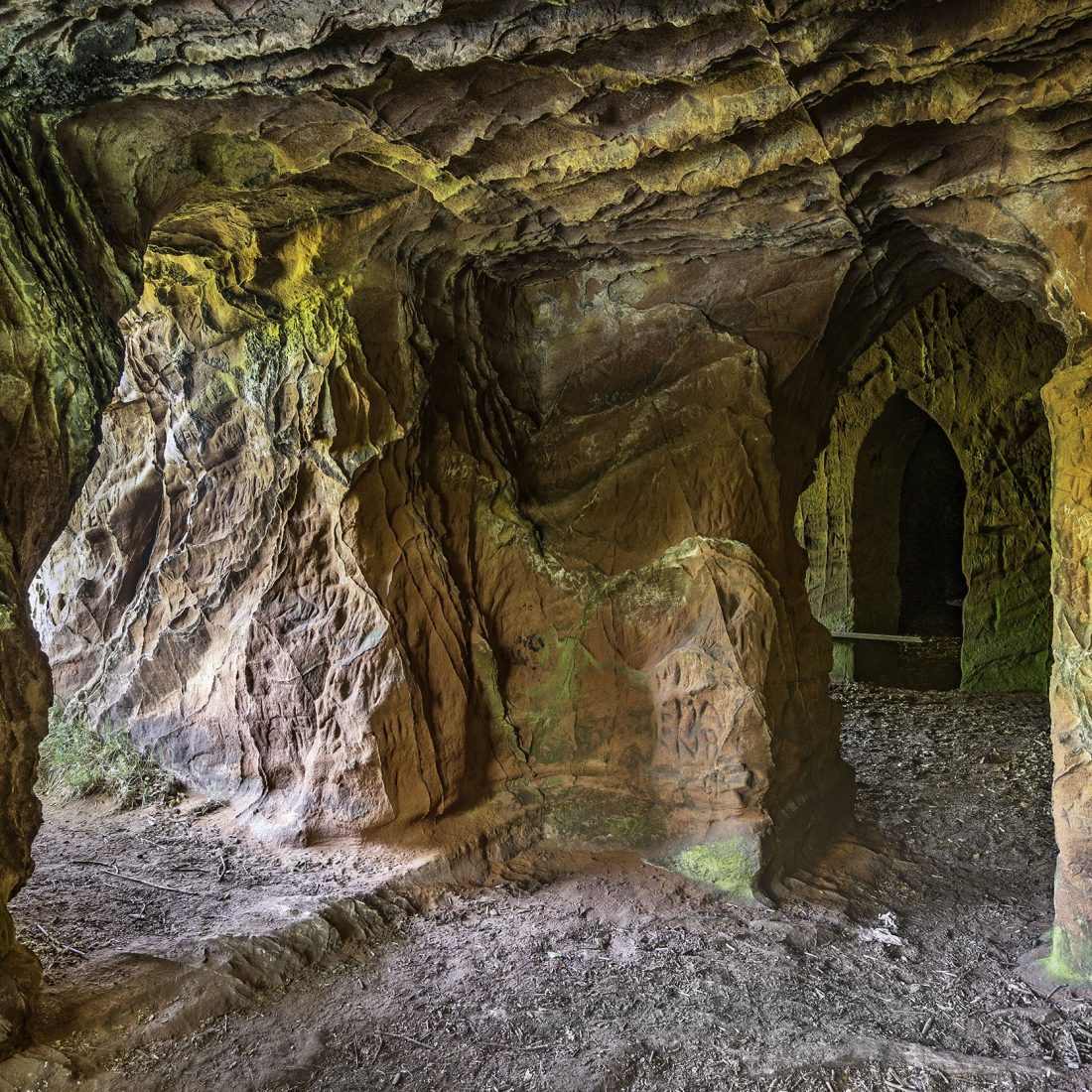 Inside of caves carved into a sandstone cliff. Shows doorways to further caves and the cliff edge.