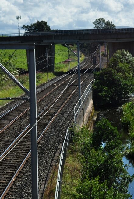 A main railway line runs from front to back of the picture. A river runs along its right-hand side ,and a motorway bridge is at the back of the image, running over both the railway and river.
