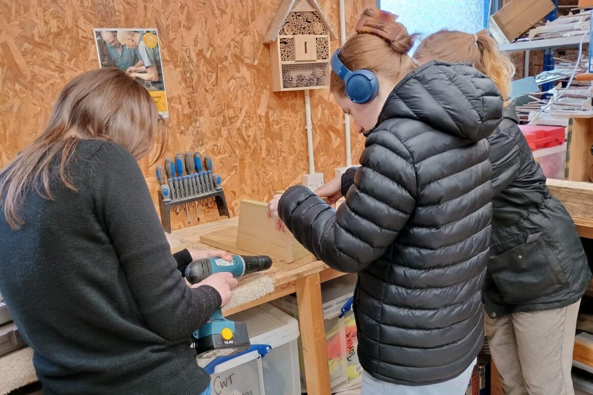 A group of young people in a woodworking workshop drilling and constructing a wooden bird box.