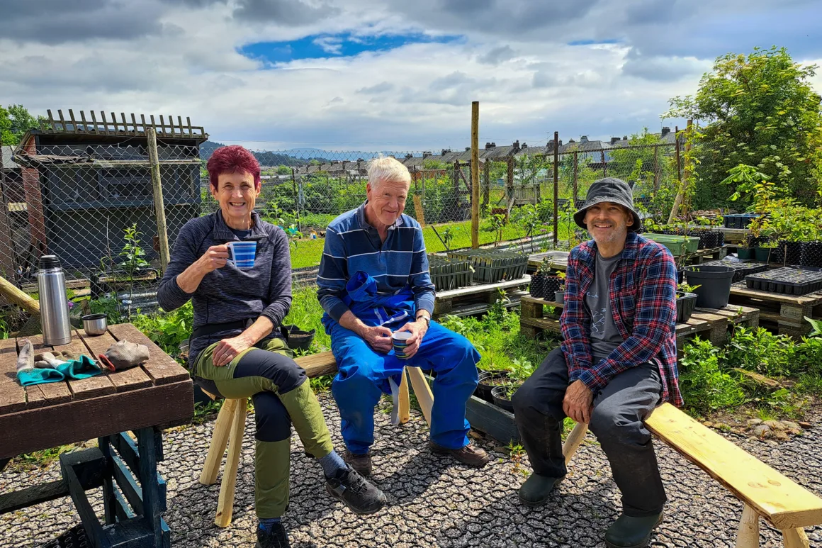 Volunteers sitting on wooden benches in sunshine, enjoying a cup of tea and a rest at the Penrith community tree nursery.