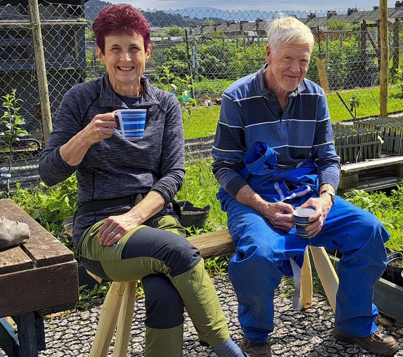 Volunteers at the Penrith community tree nursery sat on wooden benches in sunshine. Enjoying a break and enjoying a cup of tea.
