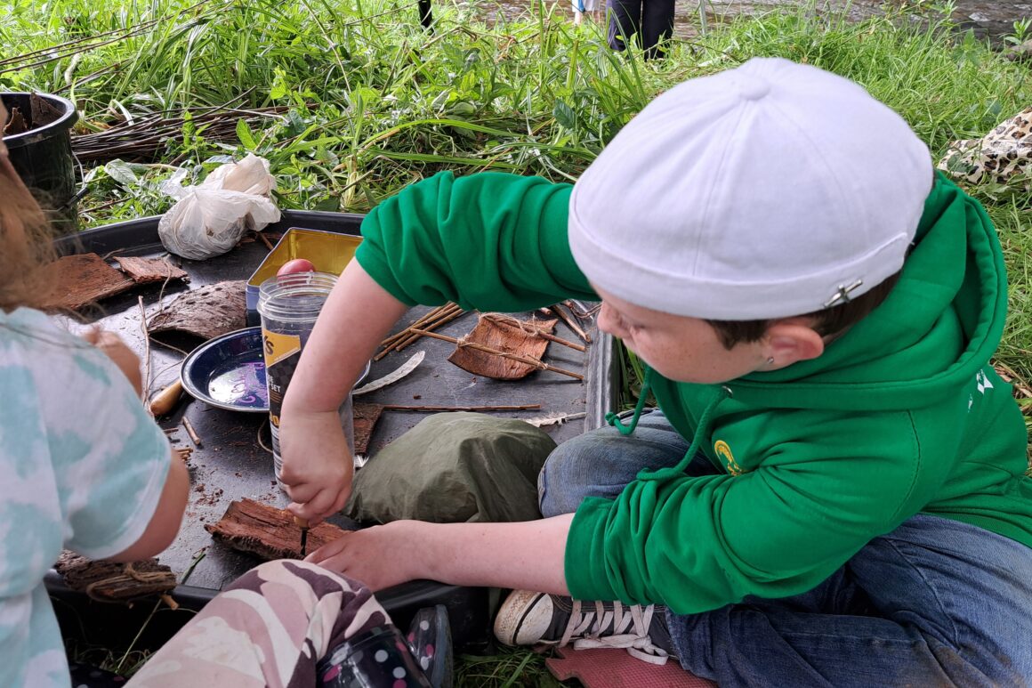 Two young people in a woodland setting leaning some woodland skills, Sat on tarpaulin with tools.