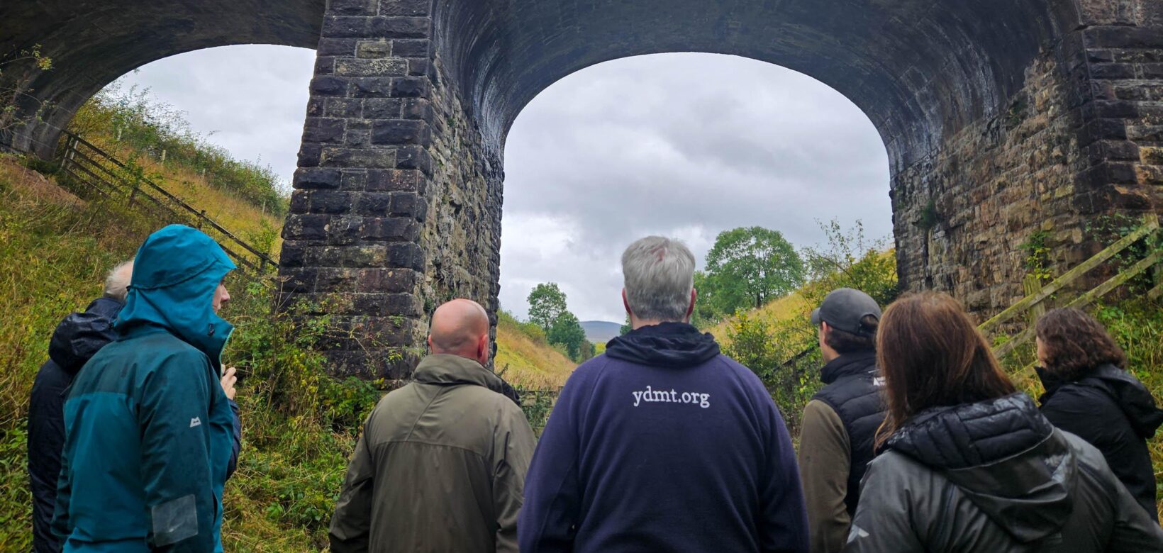 Staff members from Cumbria Wildlife Trust, Yorkshire Dale National Park Authority and Eden Rivers Trust standing on the Podgill viaduct trail path looking up at the Podgill viaduct structure.
