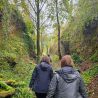 People walking along a dirt path in a hollowed-out gorge. It's Autumn, so leaves are already falling to the ground.