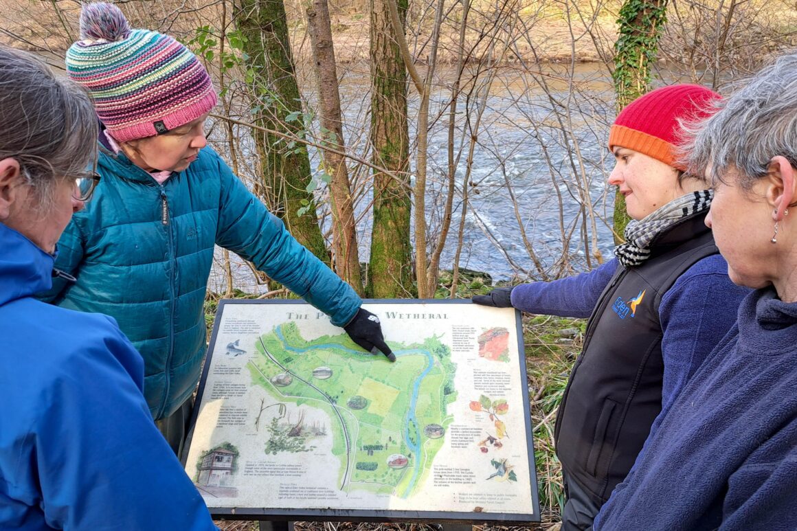 ERT staff and landowner looking at an interpretation panel on site at Wallacefield featuring a map of the Parish of Wetheral and natural and cultural points of interest.