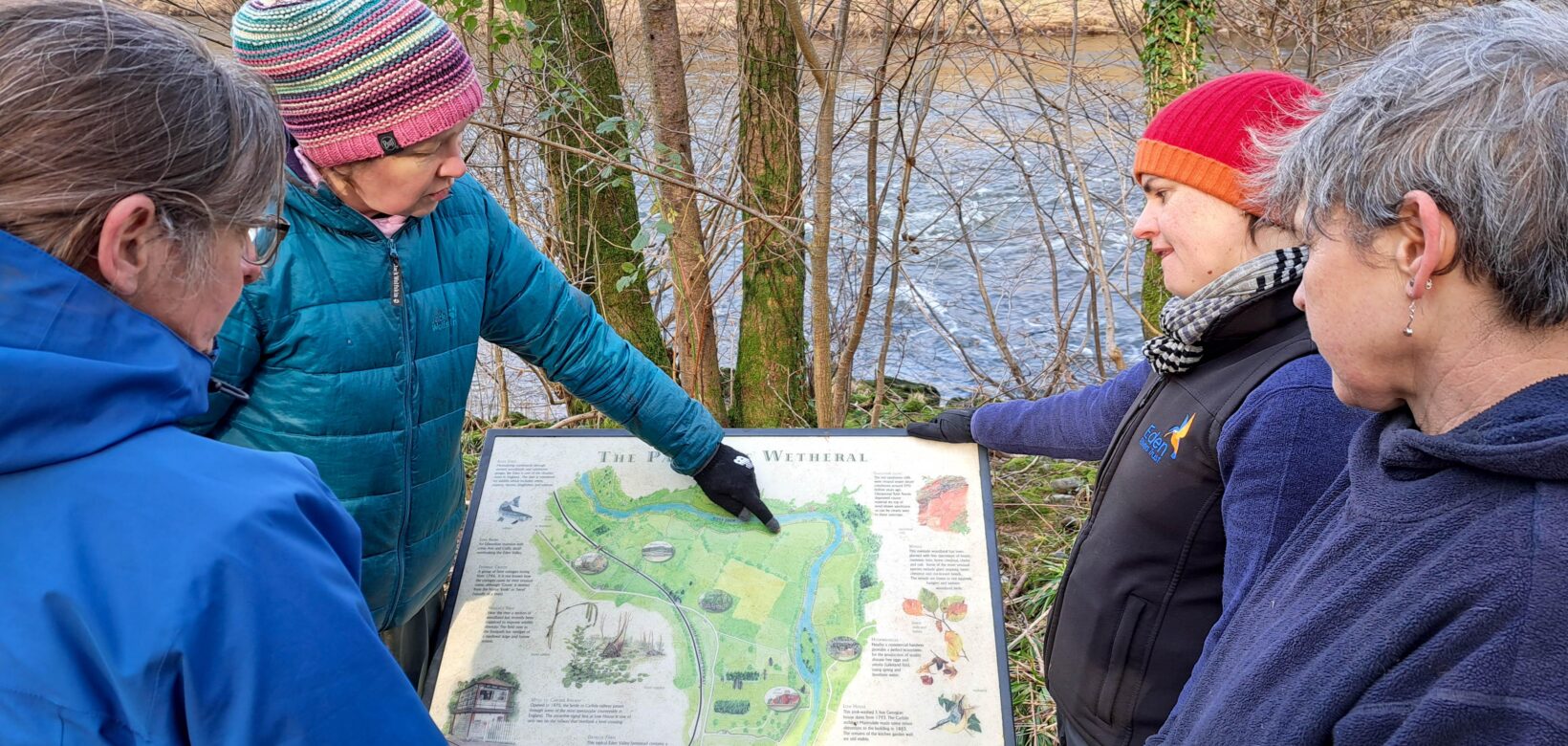 ERT staff and landowner looking at an interpretation panel on site at Wallacefield featuring a map of the Parish of Wetheral and natural and cultural points of interest.