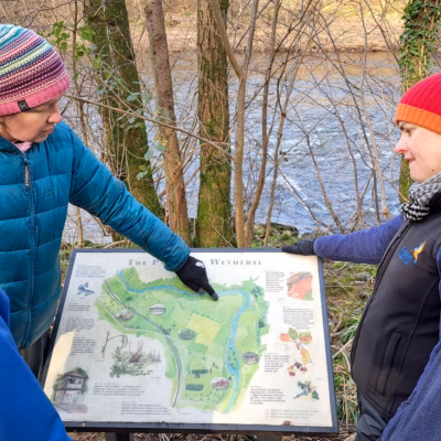 ERT staff and landowner looking at an interpretation panel on site at Wallacefield featuring a map of the Parish of Wetheral and natural and cultural points of interest.