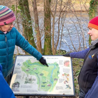 ERT staff and landowner looking at an interpretation panel on site at Wallacefield featuring a map of the Parish of Wetheral and natural and cultural points of interest.