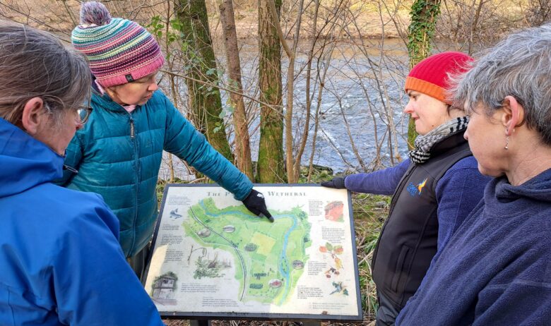 ERT staff and landowner looking at an interpretation panel on site at Wallacefield featuring a map of the Parish of Wetheral and natural and cultural points of interest.