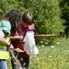 Two people are standing in grassland amongst tall meadow plants and flowers. They are inspecting the contents of butterfly nets for insects.