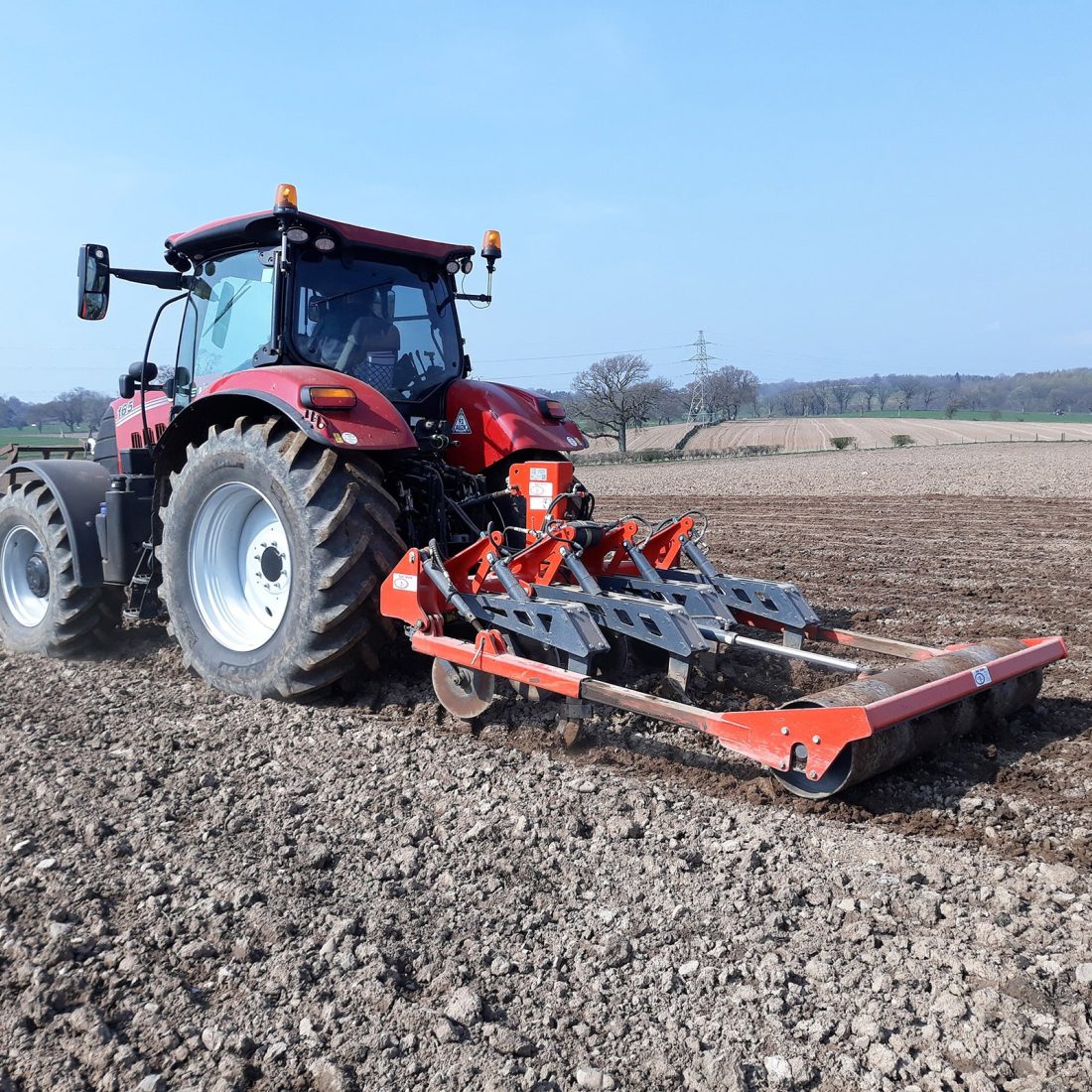 A tractor is pulling a machine called a sward lifter - it is scoring the ground and then has a roller to flatten it afterwards.