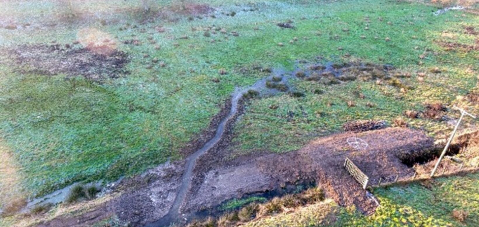 Aerial view of a water channel excavated on flat grassland.