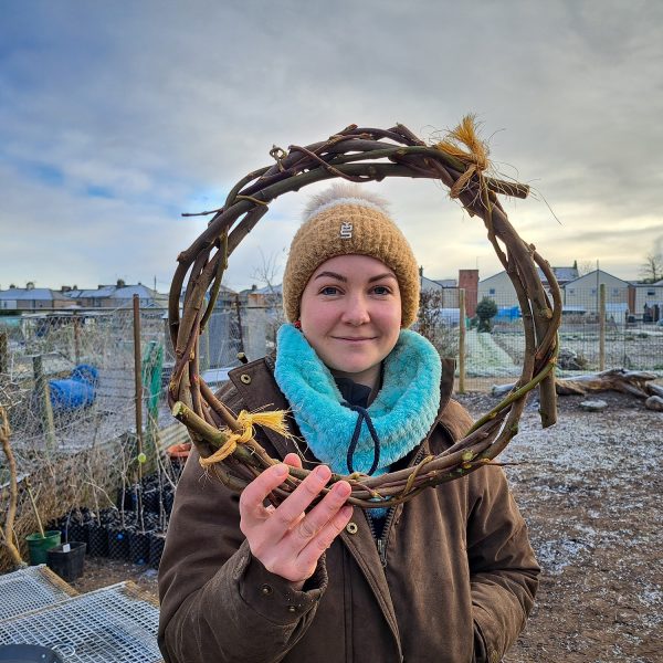 A person posing for a photograph holding up and looking through a circular weaved willow hoop.