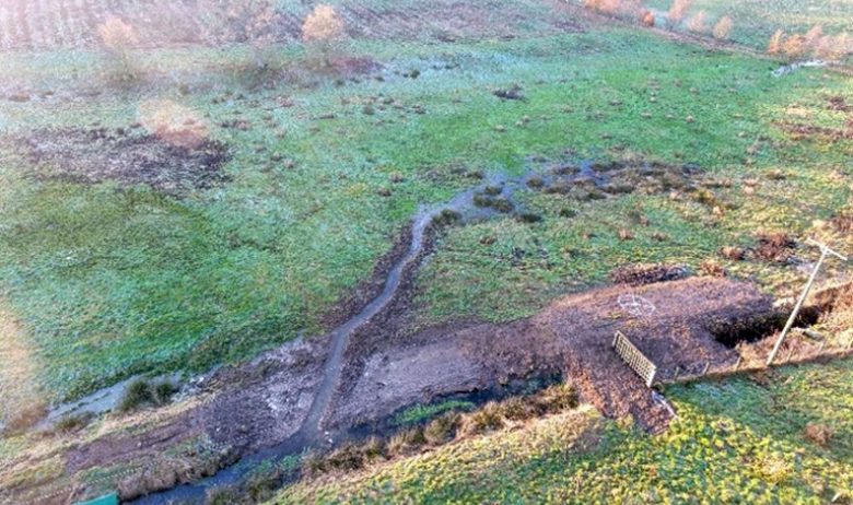 Aerial view of a water channel excavated on flat grassland.