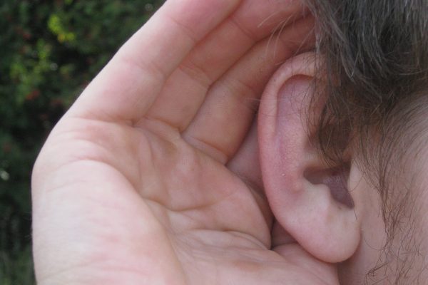 A close up of the side of a face with a hand cupping the ear to listen out for sounds.