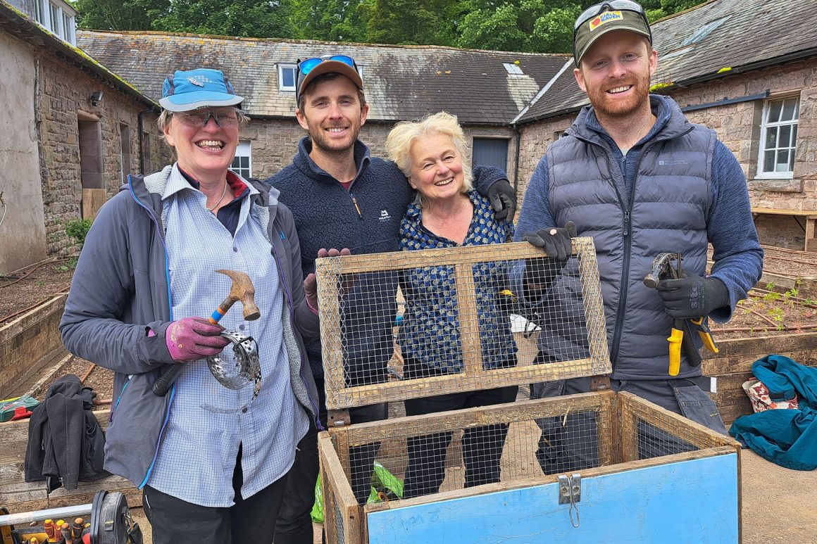 Four people stand behind a wooden cage for water voles that they have just mended.