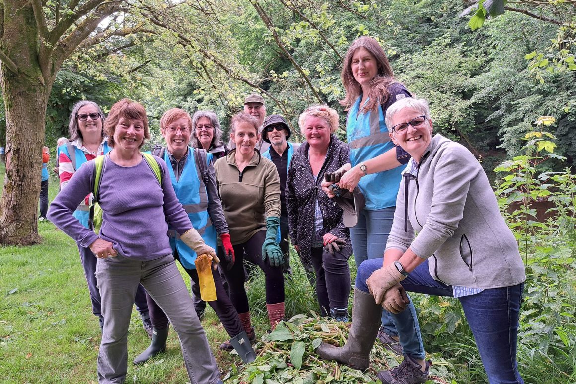 A group of women are standing behind, and on a heap of plants that have been well and truly bashed.