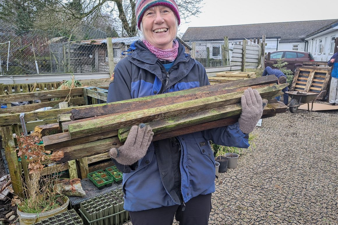 A woman is holding lots of thin lengths of wood in her arms and is smiling at the camera.