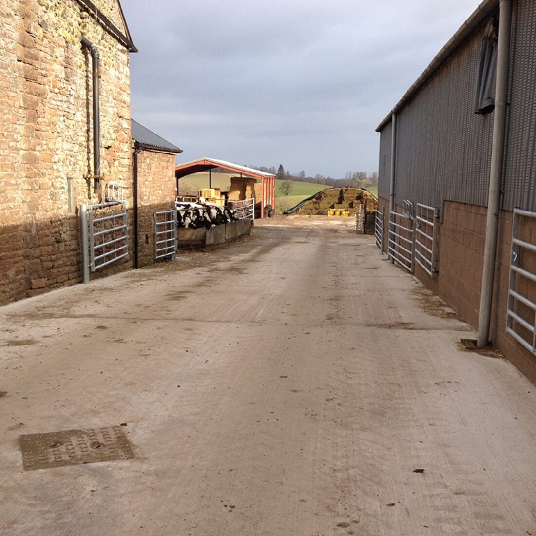 Wide stone farm yard with farm buildings to either side.