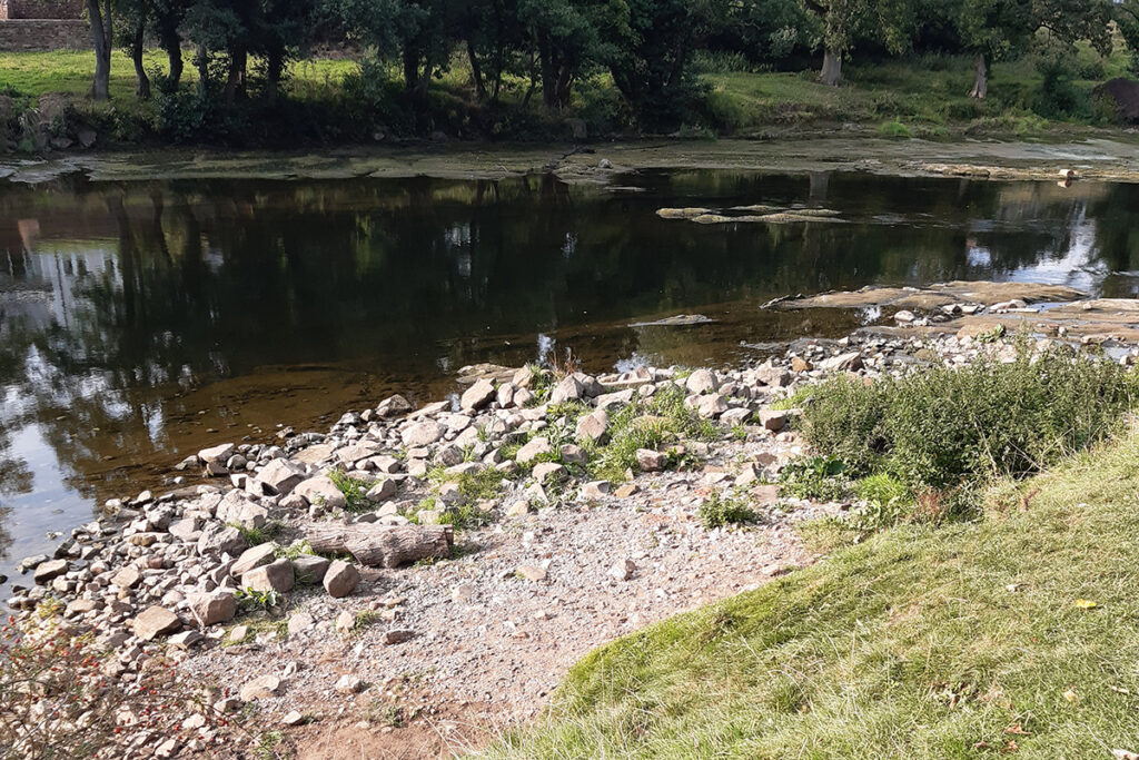 Eroded riverbank with stones and boulders by the river's edge.