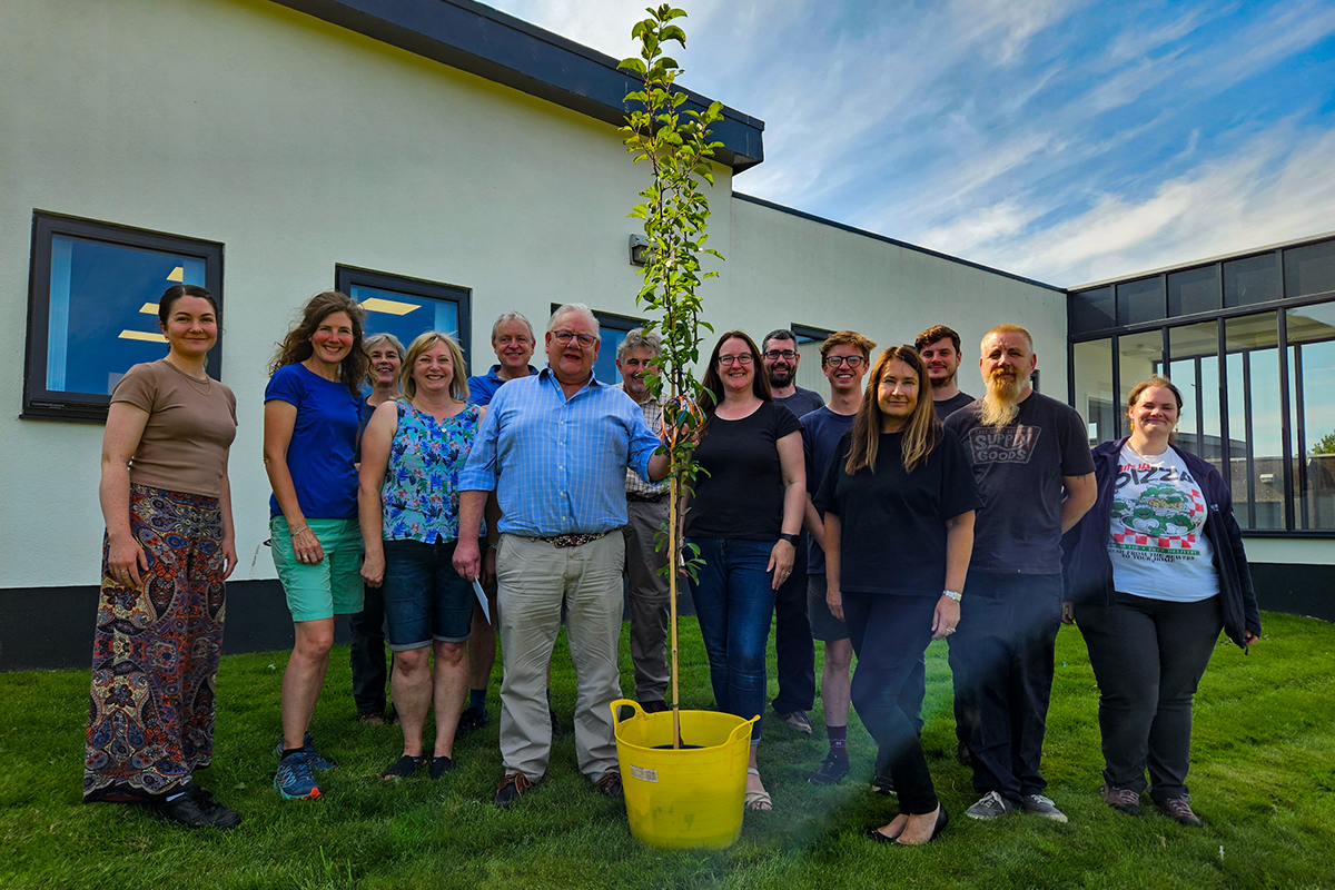 Big group of ERT staff with Charles in the middle holding onto a small tree given as a present.